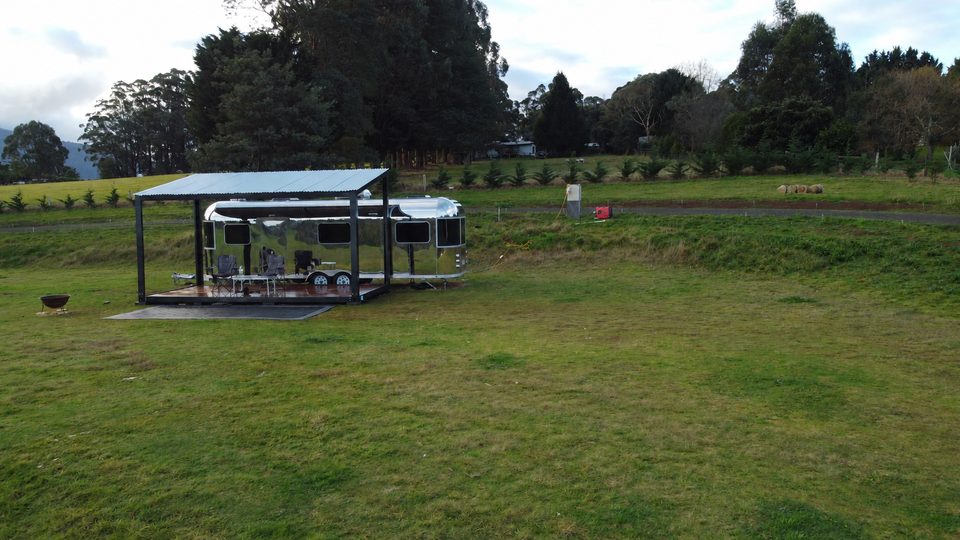 Aerial view of the silver caravan and covered pavilion in a grassy Rawson clearing